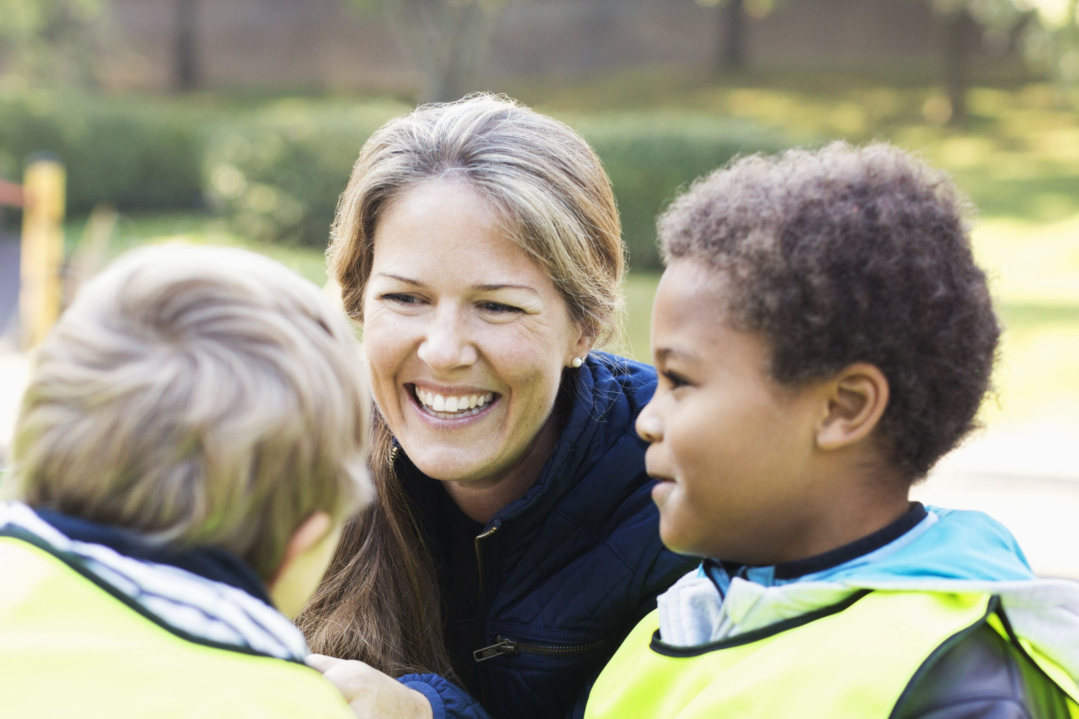 En blid kvinne snakker med to barn i refleksvester